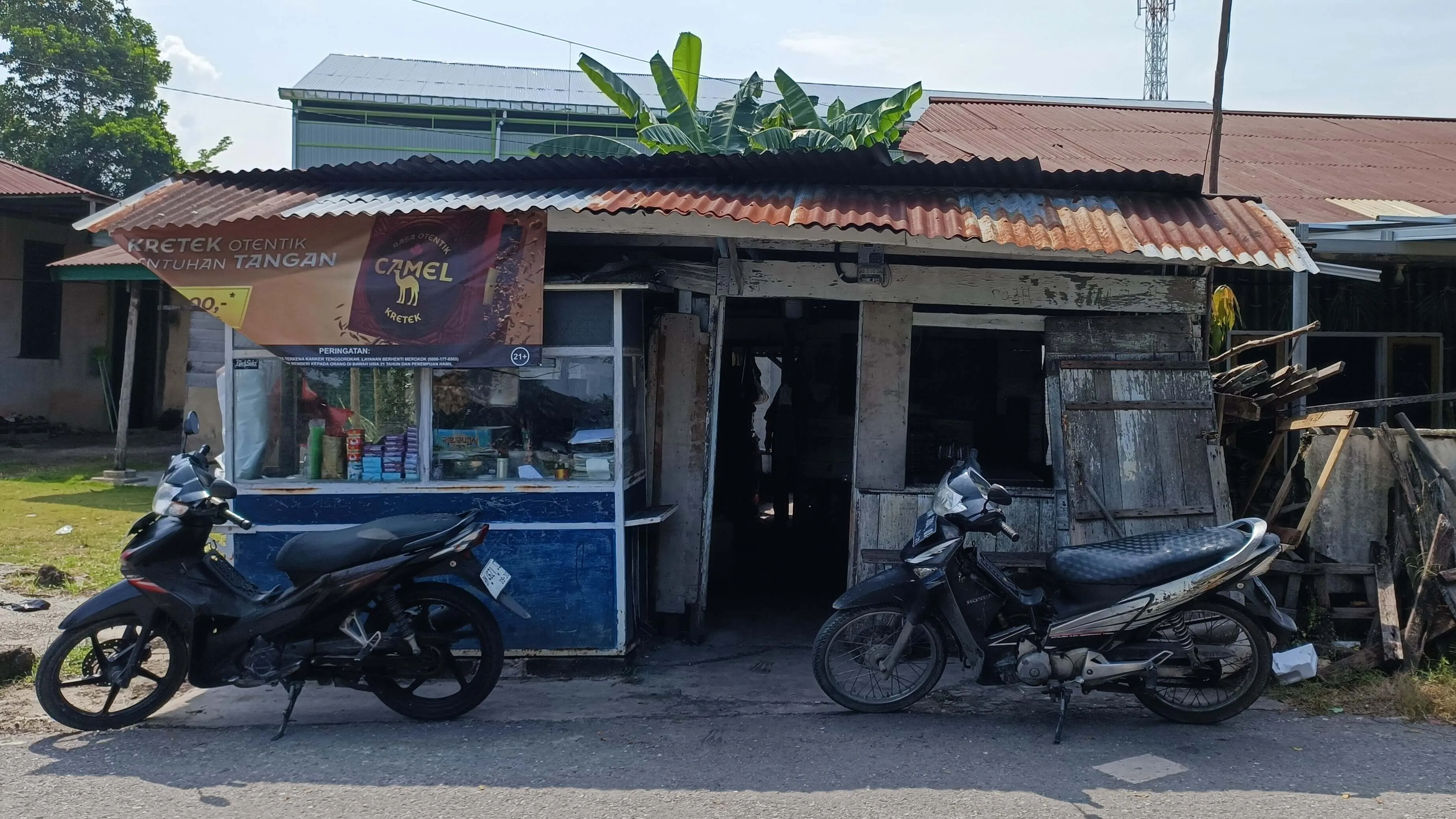 Atmospheric wide shot of a traditional Indonesian warkop with morning sunlight streaming through windows and steam rising from coffee cups on rustic wooden tables.